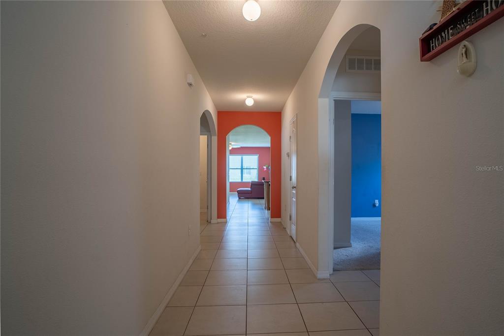 A hallway with tiled floors leads through arched doorways toward a room with orange walls — 373 ABERDEEN DRIVE, DAVENPORT, FL