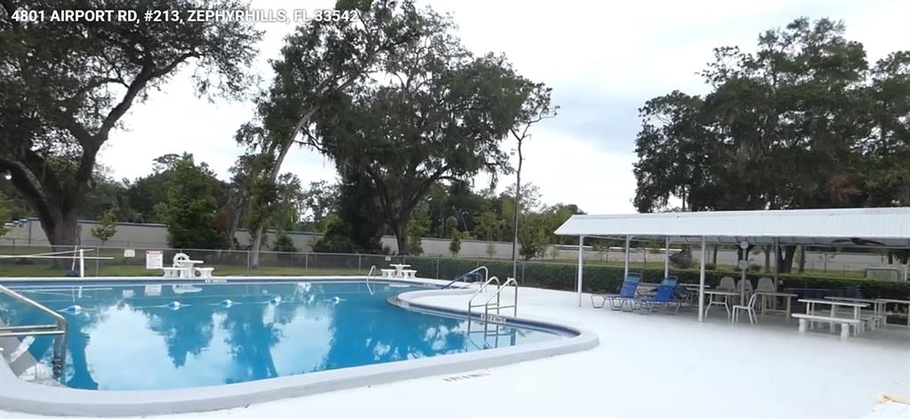 An outdoor swimming pool with a covered patio area and surrounding trees — 4801 AIRPORT ROAD UNIT 213, ZEPHYRHILLS, FL
