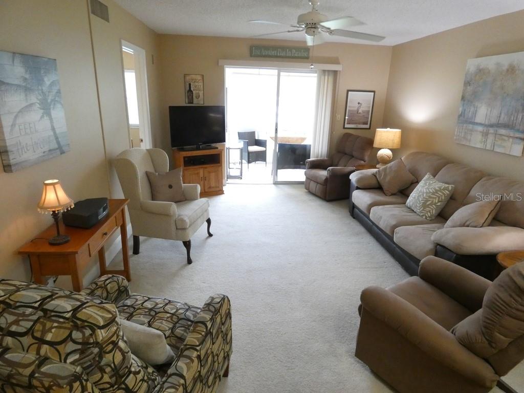 A living room features a beige sofa, patterned armchair, television, and sliding glass doors to a patio — 4801 AIRPORT ROAD UNIT 213, ZEPHYRHILLS, FL