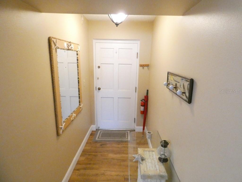 An entryway features a white door, wood-look flooring, a mirror, and a small glass table — 4801 AIRPORT ROAD UNIT 213, ZEPHYRHILLS, FL