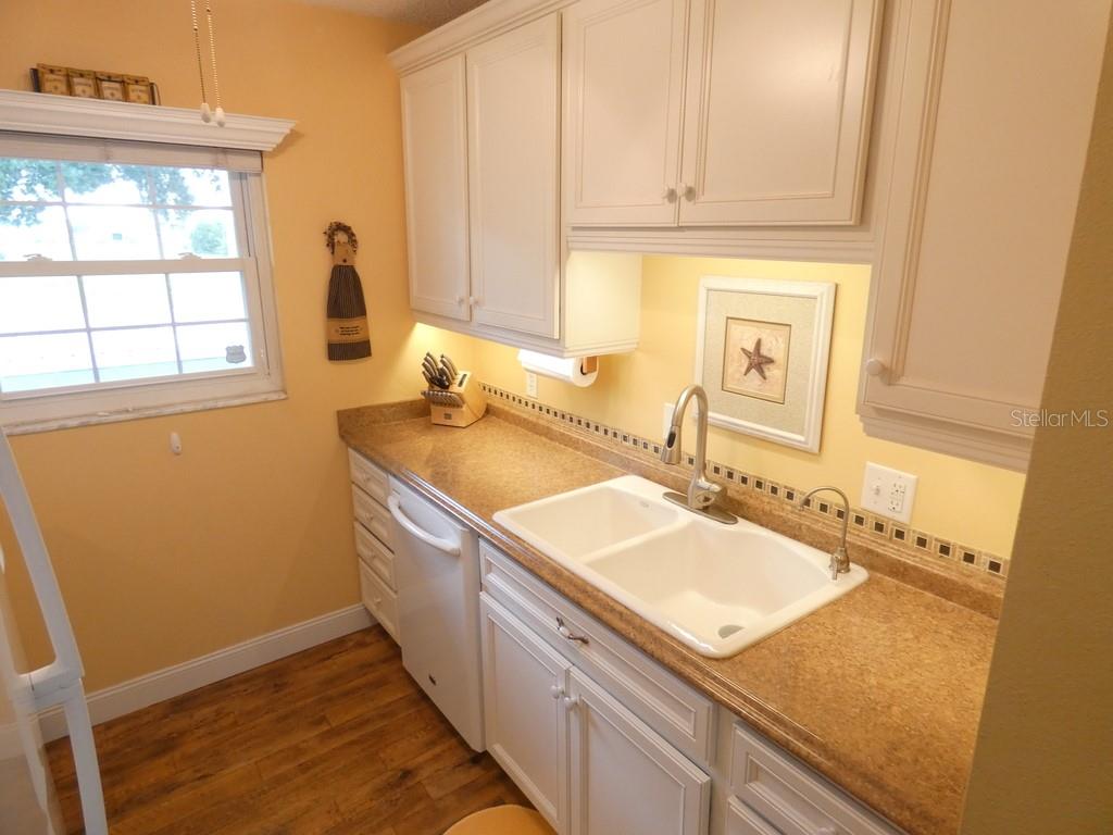 A kitchen features white cabinets, a double-basin sink, and tan countertops against yellow walls — 4801 AIRPORT ROAD UNIT 213, ZEPHYRHILLS, FL