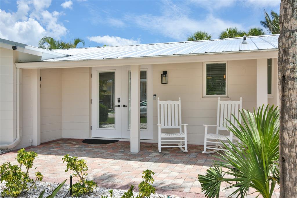 A covered patio with two white rocking chairs sits in front of a house entrance — 211 ISLAND CIRCLE, SARASOTA, FL