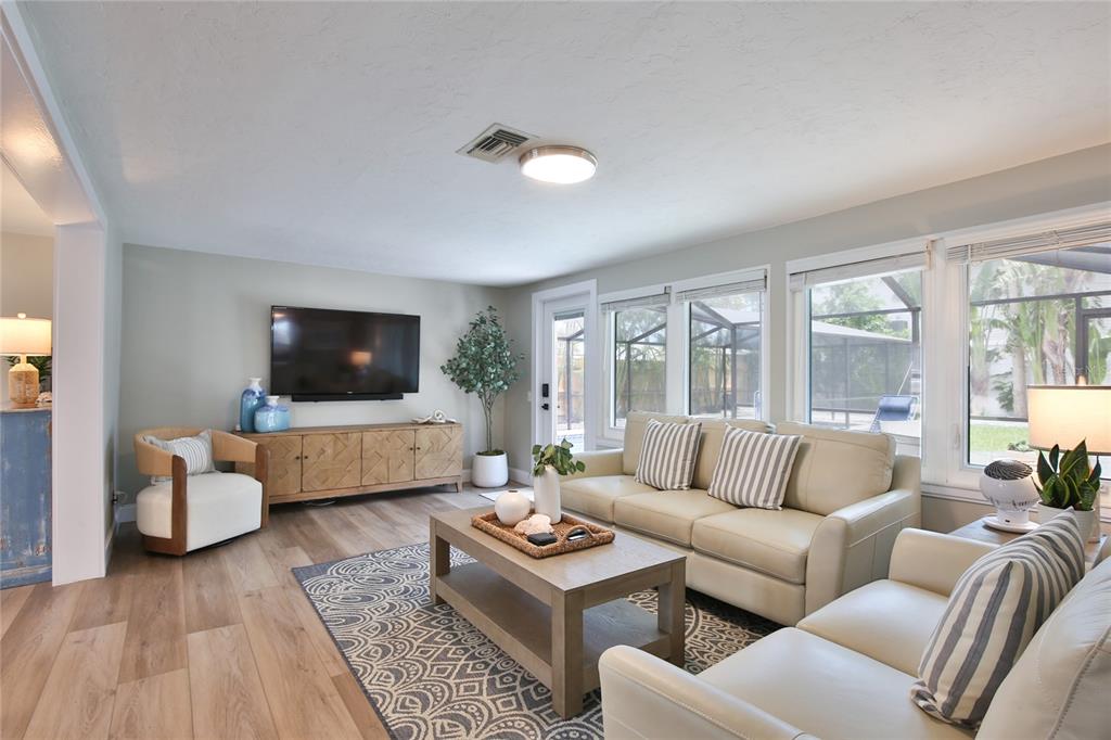 A living room features light wood flooring, a beige sofa, a patterned rug, and large windows — 211 ISLAND CIRCLE, SARASOTA, FL