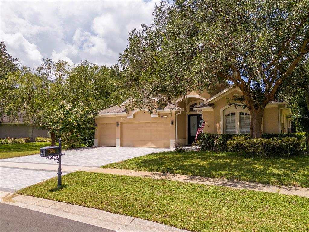 A tan single-story house with a three-car garage and a paved driveway under large trees — 10301 OAKVIEW POINTE TERRACE, GOTHA, FL