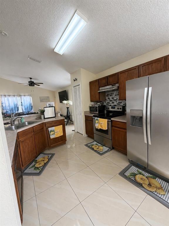 A kitchen features wood cabinets, stainless steel appliances, and light-colored tile flooring — 3843 WEETAMOO CIRCLE, ORLANDO, FL