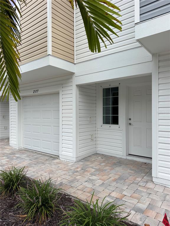 The exterior of a townhouse features a white garage door, a front door, and paved walkway — 2577 6TH AVENUE DRIVE E, BRADENTON, FL