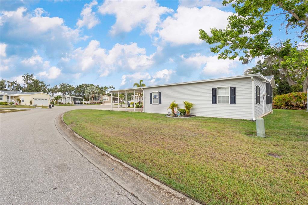A light-colored manufactured home with a carport sits on a corner lot along a street — 3421 70TH AVENUE E, ELLENTON, FL