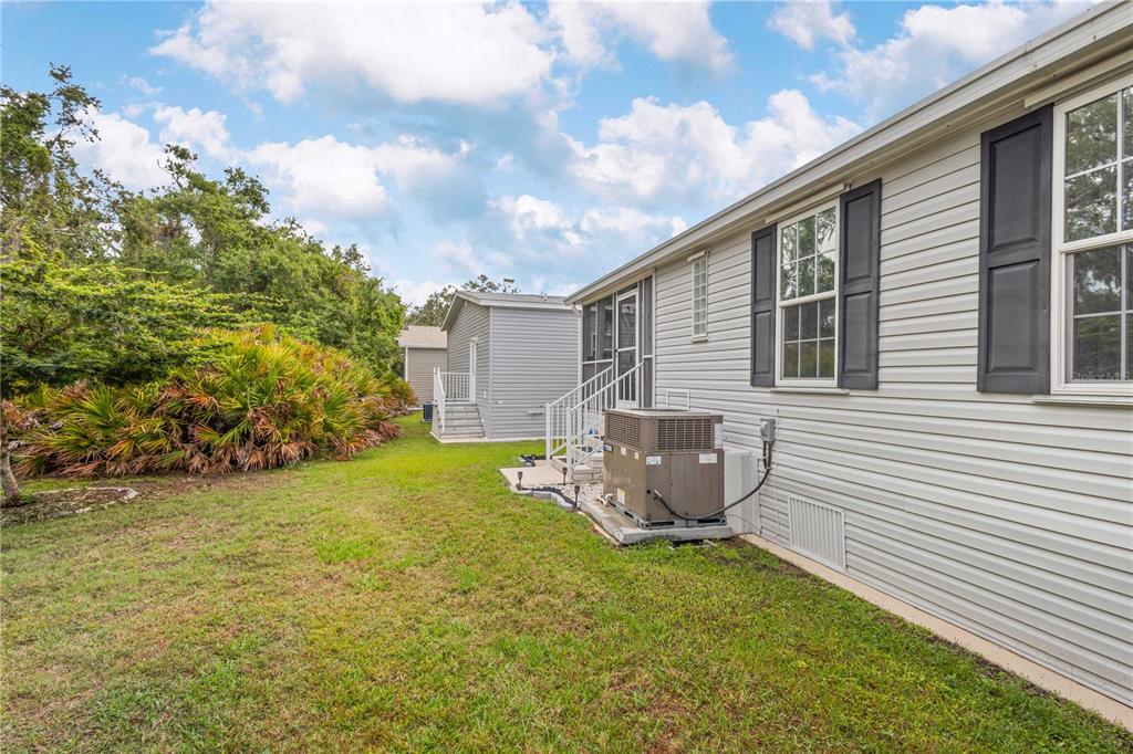 The exterior side of a light-colored house features a central air conditioning unit and lawn — 3421 70TH AVENUE E, ELLENTON, FL