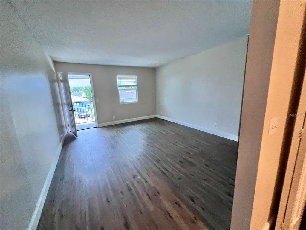 An empty room features wood-look flooring, light-colored walls, a window, and a door to a balcony — 4170 BARNA AVENUE UNIT F, TITUSVILLE, FL