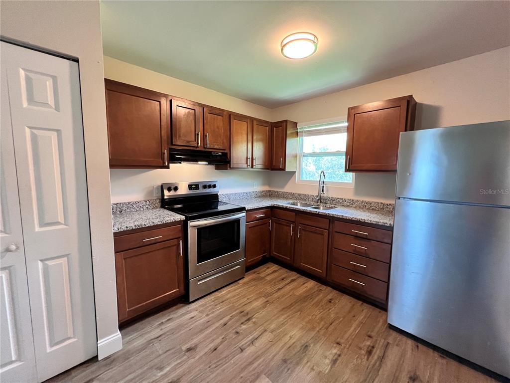 A kitchen features wood cabinets, granite countertops, stainless steel appliances, and wood-look flooring — 4170 BARNA AVENUE UNIT F, TITUSVILLE, FL