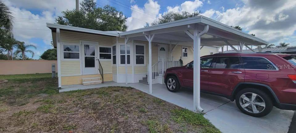 A light yellow mobile home features a white carport and a red SUV parked underneath — 5208 5TH B STREET E, BRADENTON, FL