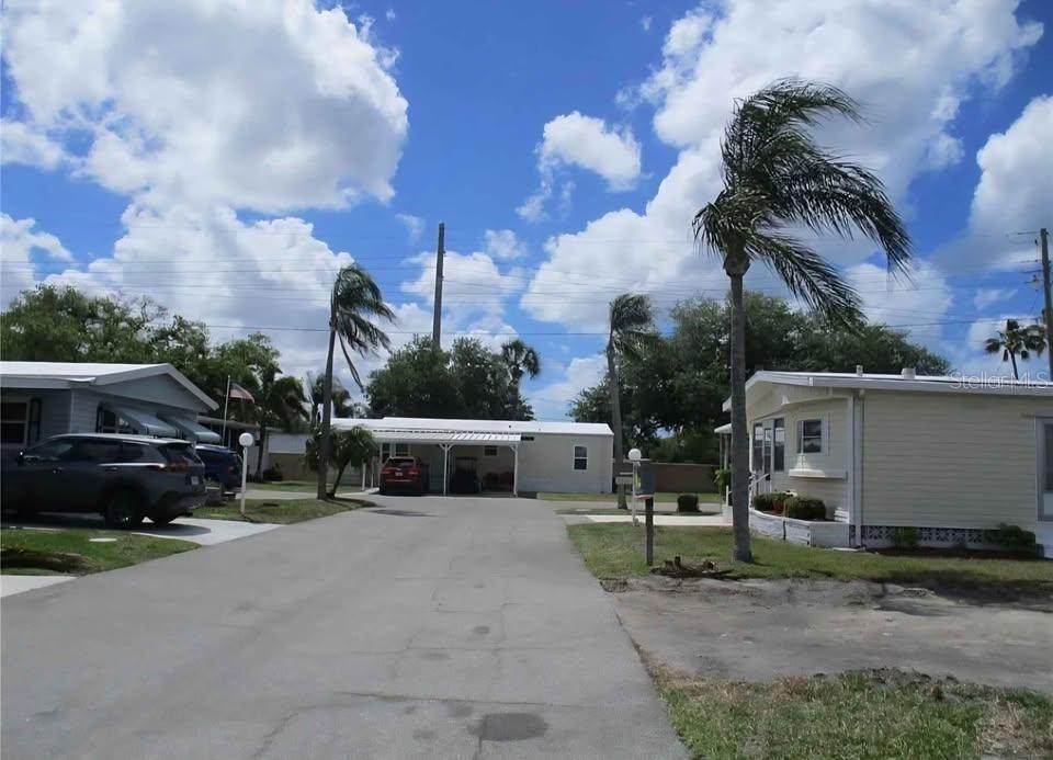 A paved driveway leads to a white manufactured home with a carport under a blue sky — 5208 5TH B STREET E, BRADENTON, FL