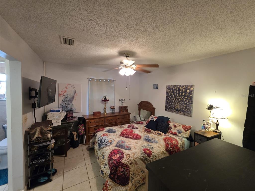 A bedroom features a bed with patterned bedding, a wooden dresser, and a ceiling fan — 5045 MISTY LAKE DRIVE, MULBERRY, FL