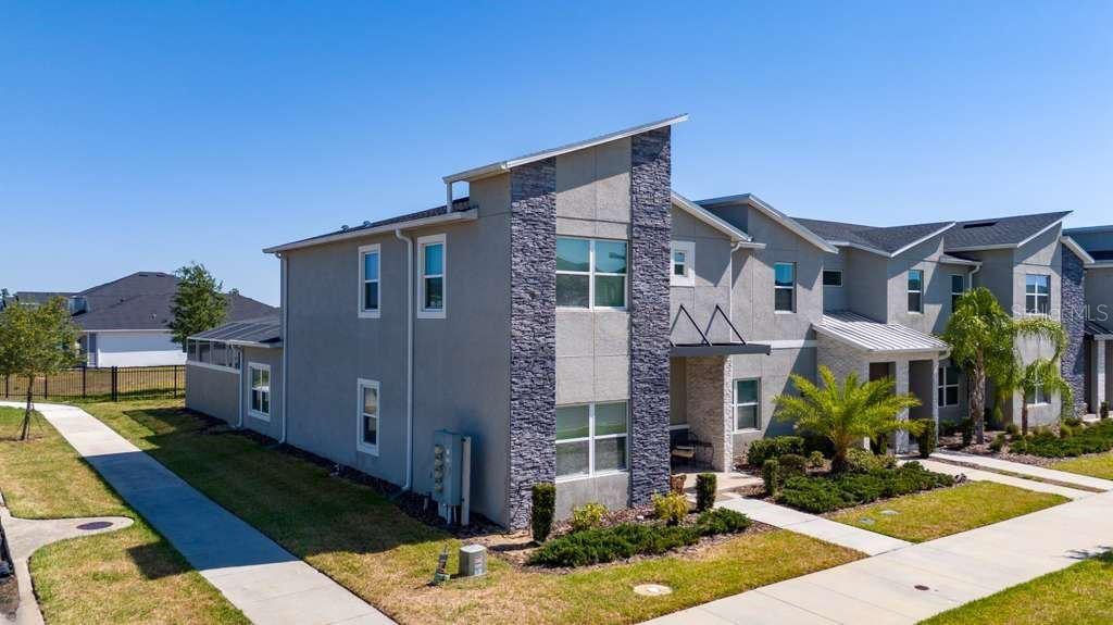 A modern two-story townhouse features a stone-accented facade and a metal-roofed entryway — 8999 CABOT CLIFFS DRIVE, DAVENPORT, FL