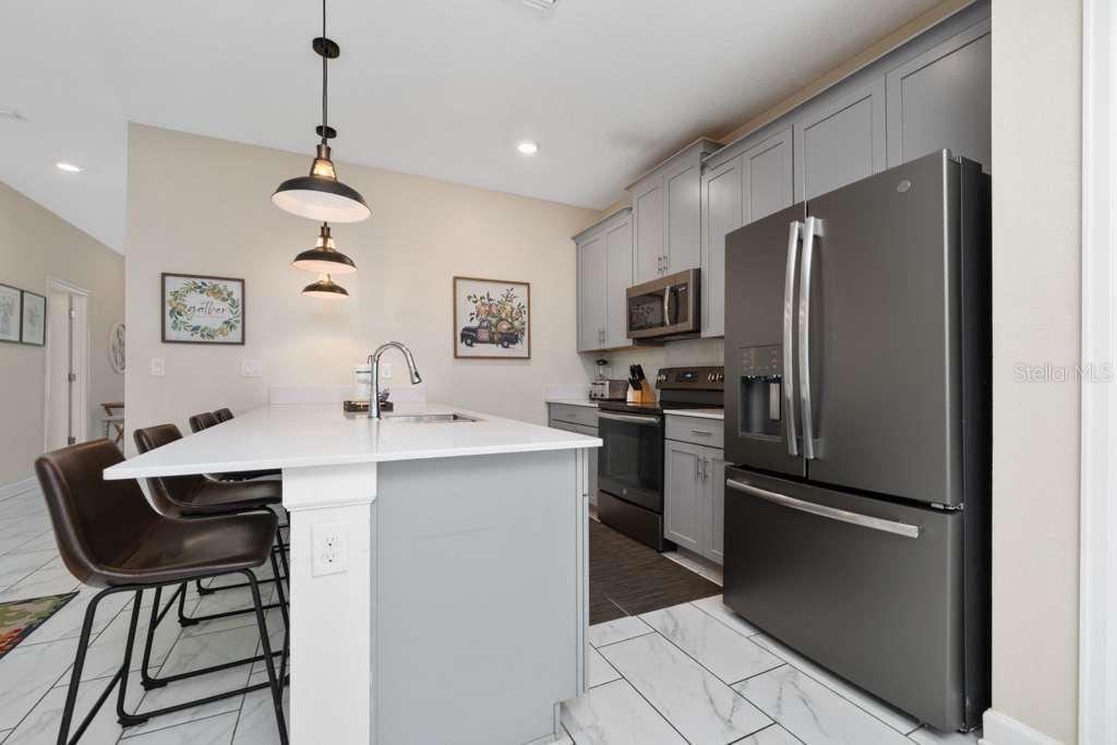 A kitchen features gray cabinets, stainless steel appliances, a white island, and marble-look tile flooring — 8999 CABOT CLIFFS DRIVE, DAVENPORT, FL
