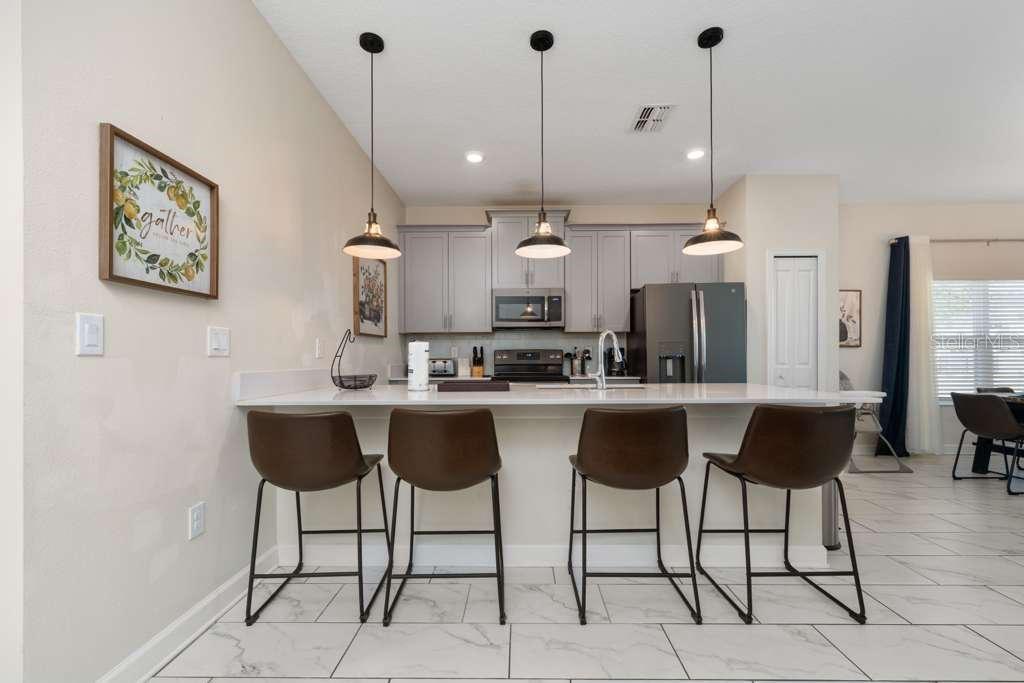 A kitchen features gray cabinets, a white island with four barstools, and three pendant lights — 8999 CABOT CLIFFS DRIVE, DAVENPORT, FL