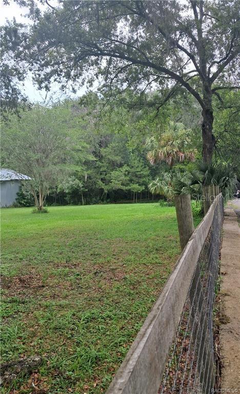 A grassy yard bordered by a wooden fence and mature trees under an overcast sky — 130TH STREET, BELLEVIEW, FL