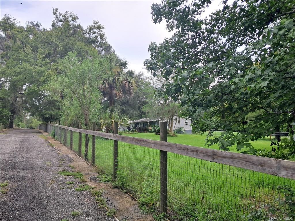 A gravel driveway runs alongside a wooden fence bordering a grassy yard and house — 130TH STREET, BELLEVIEW, FL