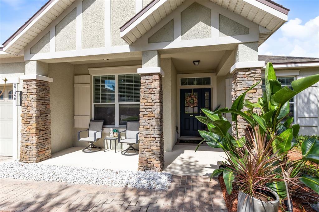 A covered front porch features stone pillars, two chairs, and a dark blue front door — 8126 CRUSHED PEPPER AVENUE, ORLANDO, FL