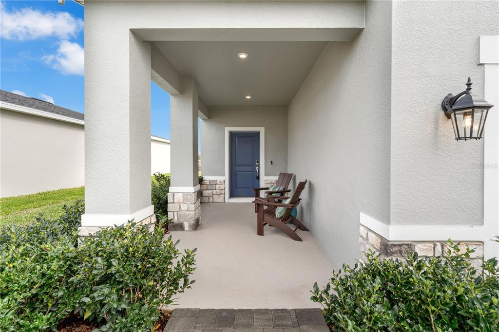 A covered front porch features a blue door, two wooden chairs, and stone accents — 10139 MORNING MEADOWLARK TRAIL, PARRISH, FL