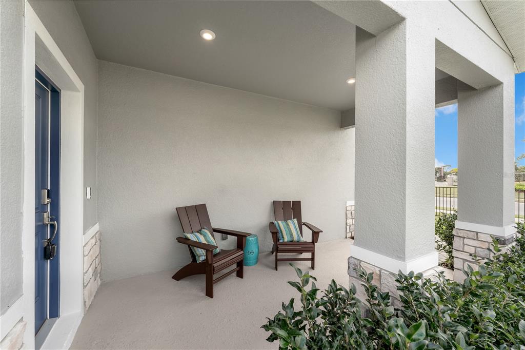 A covered front porch features two dark wooden chairs, a small blue stool, and stone accents — 10139 MORNING MEADOWLARK TRAIL, PARRISH, FL