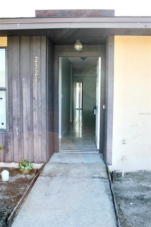 A concrete walkway leads to an open front door revealing a tiled interior hallway — 2321 TRINIDAD COURT, KISSIMMEE, FL