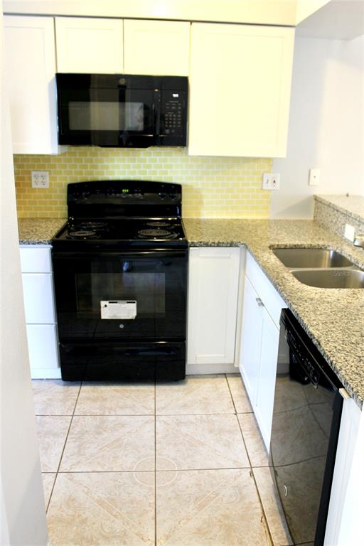A kitchen features white cabinets, black appliances, granite countertops, and a yellow tiled backsplash — 2321 TRINIDAD COURT, KISSIMMEE, FL