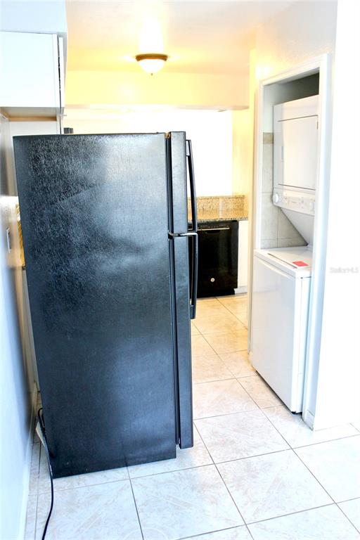 A kitchen features a black refrigerator, a stacked washer-dryer unit, and tiled flooring — 2321 TRINIDAD COURT, KISSIMMEE, FL