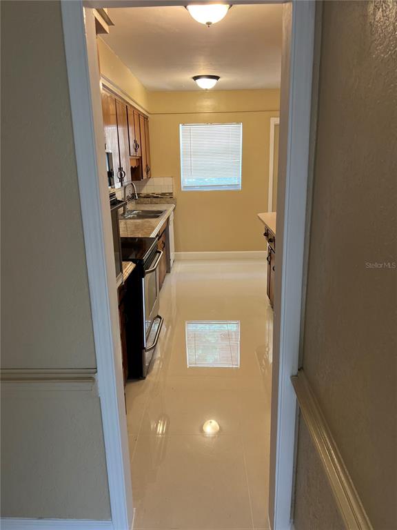 A galley kitchen features wood cabinets, stainless steel appliances, and light-colored tile flooring — 5847 HARRINGTON DRIVE, ORLANDO, FL