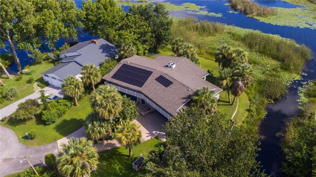 An aerial view of a house with solar panels, surrounded by trees and a waterway — 3 SE OCALE WAY, SUMMERFIELD, FL