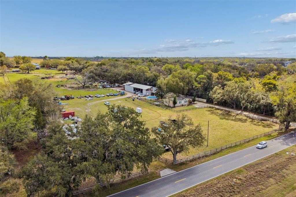 An aerial view shows a rural property with a house, a large workshop, and vehicles — 8302 WIRE ROAD, ZEPHYRHILLS, FL