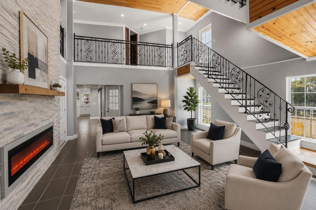A two-story living room features a stone fireplace, a staircase with iron railings, and furniture — 5414 RIVERSIDE DRIVE, PORT ORANGE, FL
