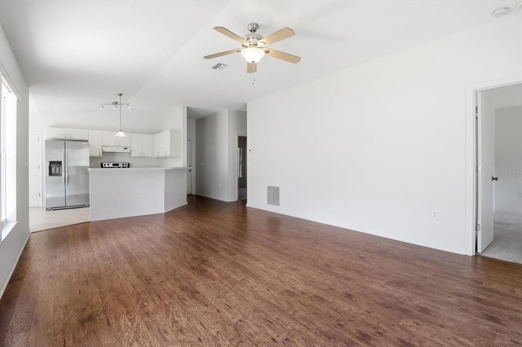 A bright living room with wood-look flooring opens to a kitchen with white cabinetry — 826 W COCKATIEL LOOP, HERNANDO, FL