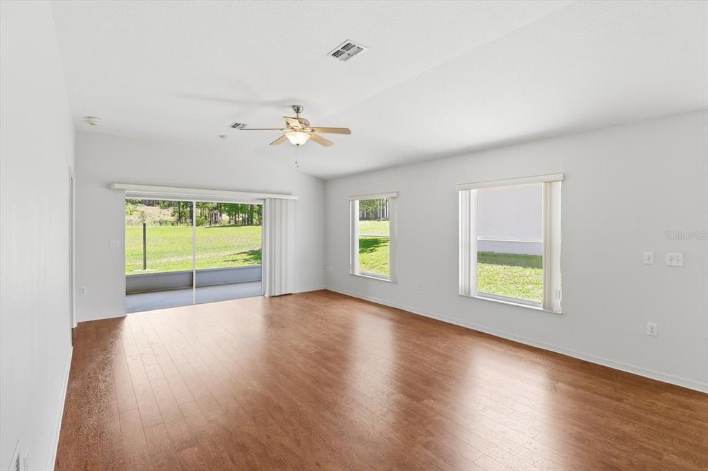 An empty living room features wood-look flooring, a ceiling fan, and sliding glass doors — 826 W COCKATIEL LOOP, HERNANDO, FL
