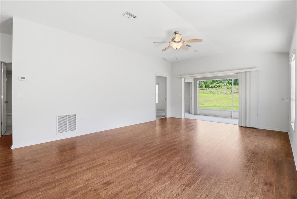 An empty living room features white walls, wood-look flooring, a ceiling fan, and sliding doors — 826 W COCKATIEL LOOP, HERNANDO, FL