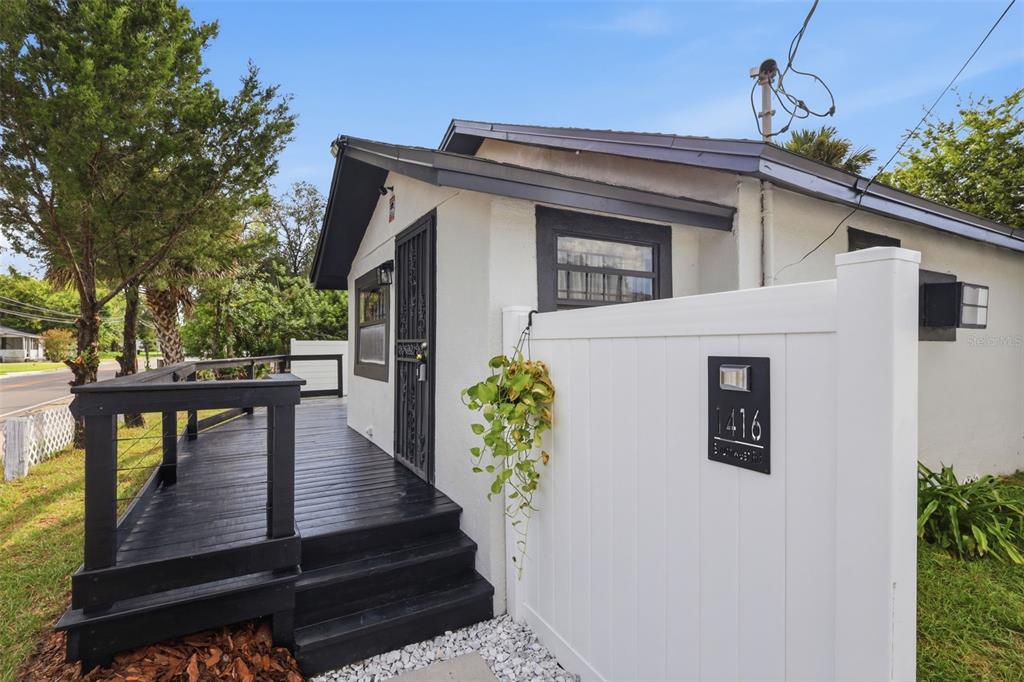 A white house exterior features a black wooden deck, a front door, and a privacy fence — 1416 SOUTHWEST ROAD, SANFORD, FL