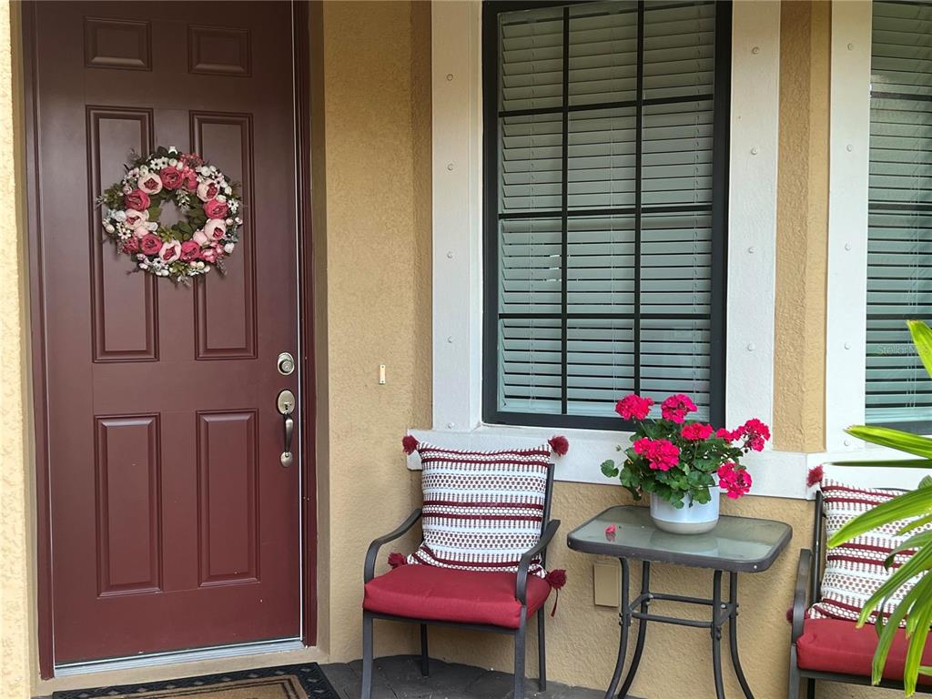 A front porch features a dark red door, two chairs with cushions, and a small table — 13737 MESSINA LOOP UNIT 101, BRADENTON, FL