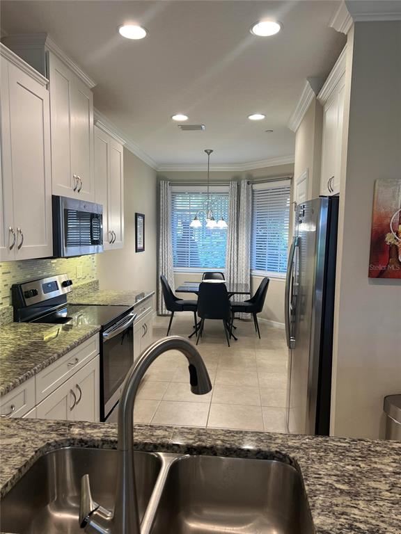 A kitchen with white cabinets, granite countertops, and stainless steel appliances overlooks a dining area — 13737 MESSINA LOOP UNIT 101, BRADENTON, FL