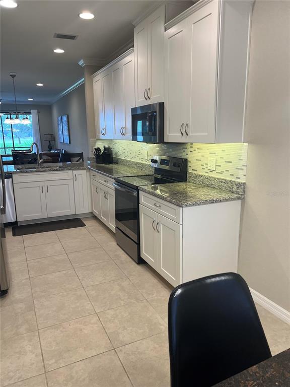 A kitchen features white cabinets, granite countertops, stainless steel appliances, and a tiled floor — 13737 MESSINA LOOP UNIT 101, BRADENTON, FL