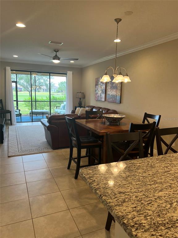 An open-concept living and dining area features tile floors, a granite island, and sliding glass doors — 13737 MESSINA LOOP UNIT 101, BRADENTON, FL