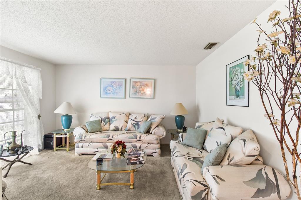 A living room features two floral sofas, a glass coffee table, and beige carpeting — 8657 CROSSBAY DRIVE, ORLANDO, FL