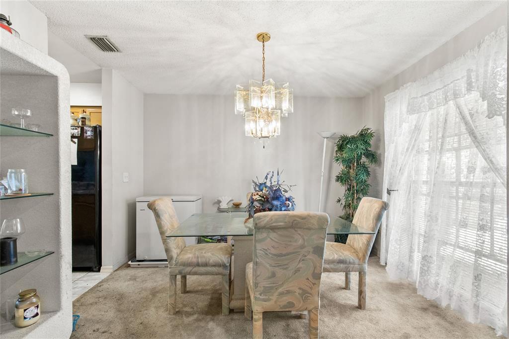 A dining room features a glass-top table, patterned chairs, a crystal chandelier, and carpeted flooring — 8657 CROSSBAY DRIVE, ORLANDO, FL