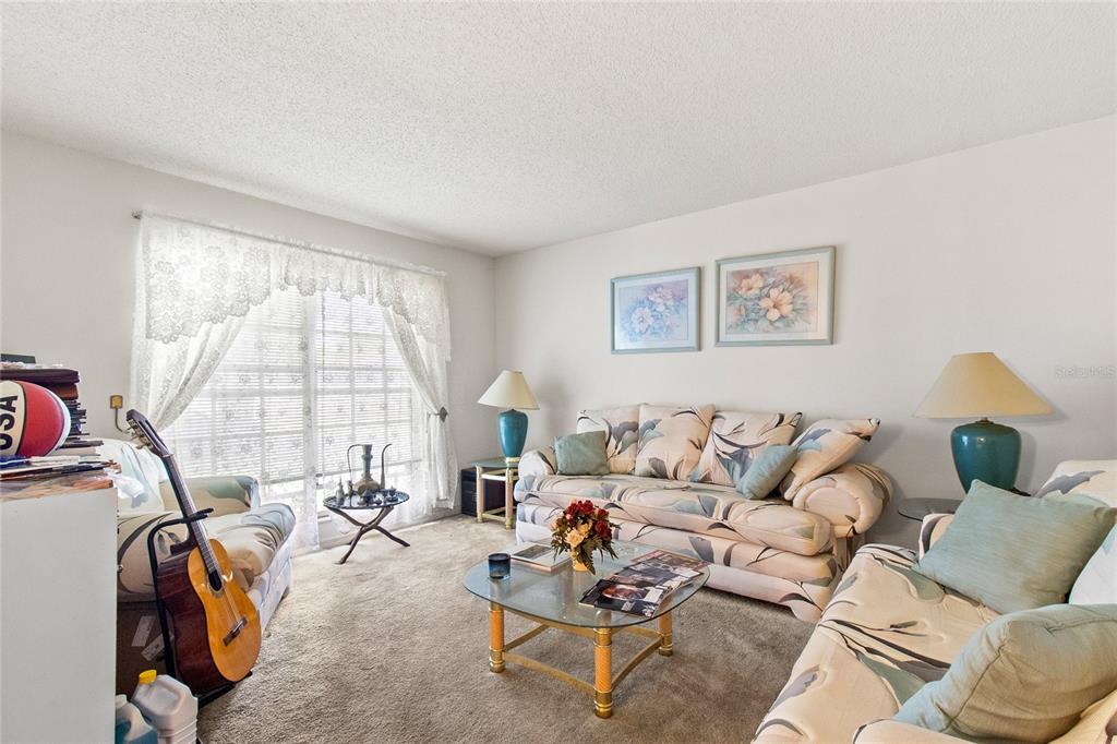 A living room features a patterned sofa, a glass coffee table, and a guitar — 8657 CROSSBAY DRIVE, ORLANDO, FL