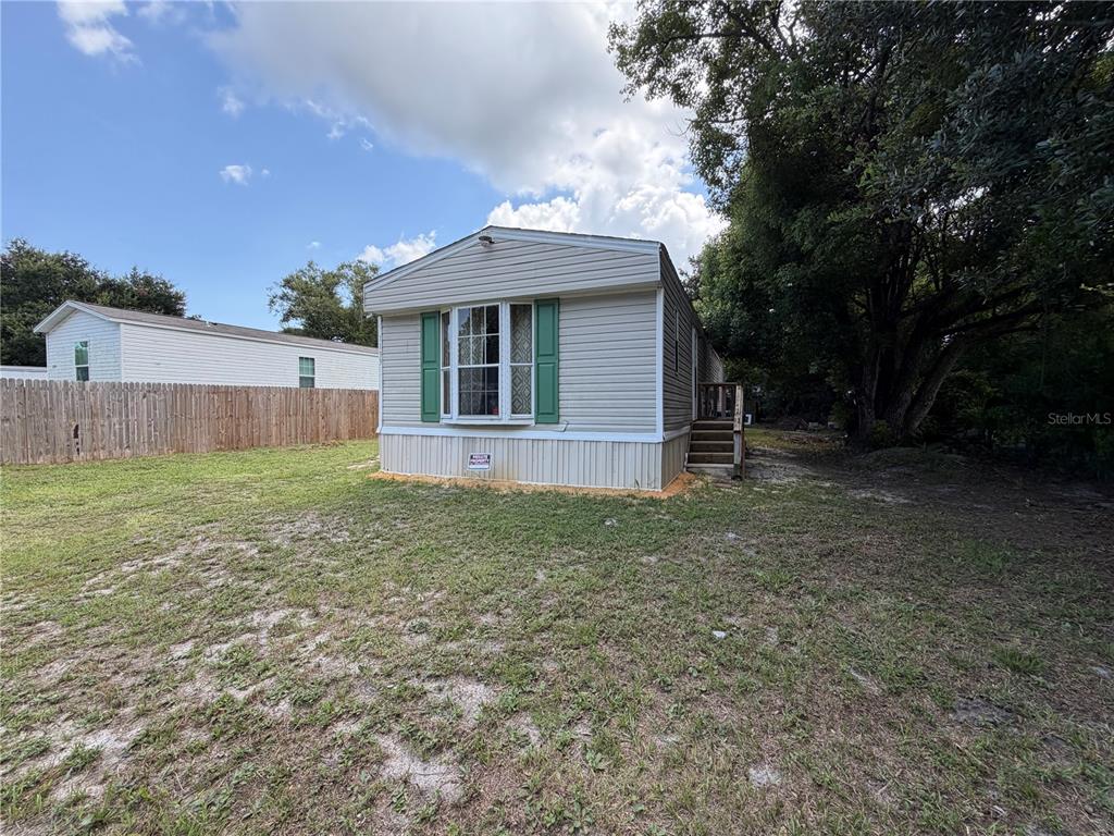 A single-story manufactured home with beige siding and green shutters sits on a grassy lot — 1133 AVENUE G, ORMOND BEACH, FL