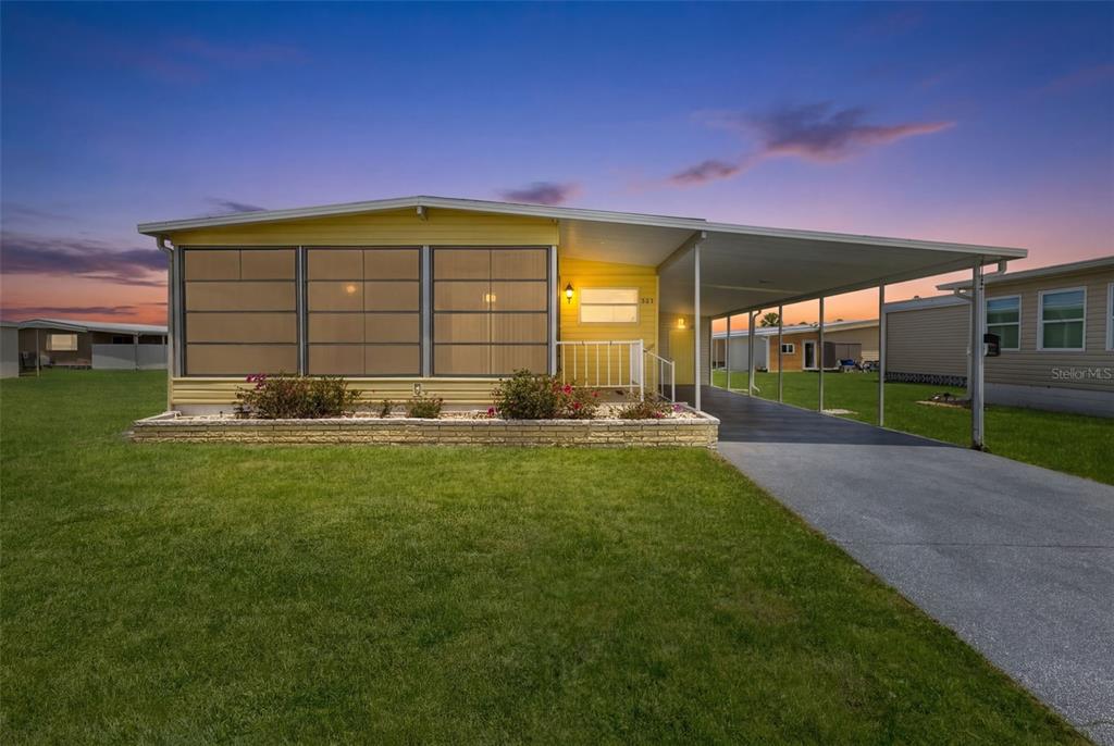 A yellow manufactured home features a screened-in front porch, a carport, and a brick planter — 322 ROBALO, NORTH PORT, FL