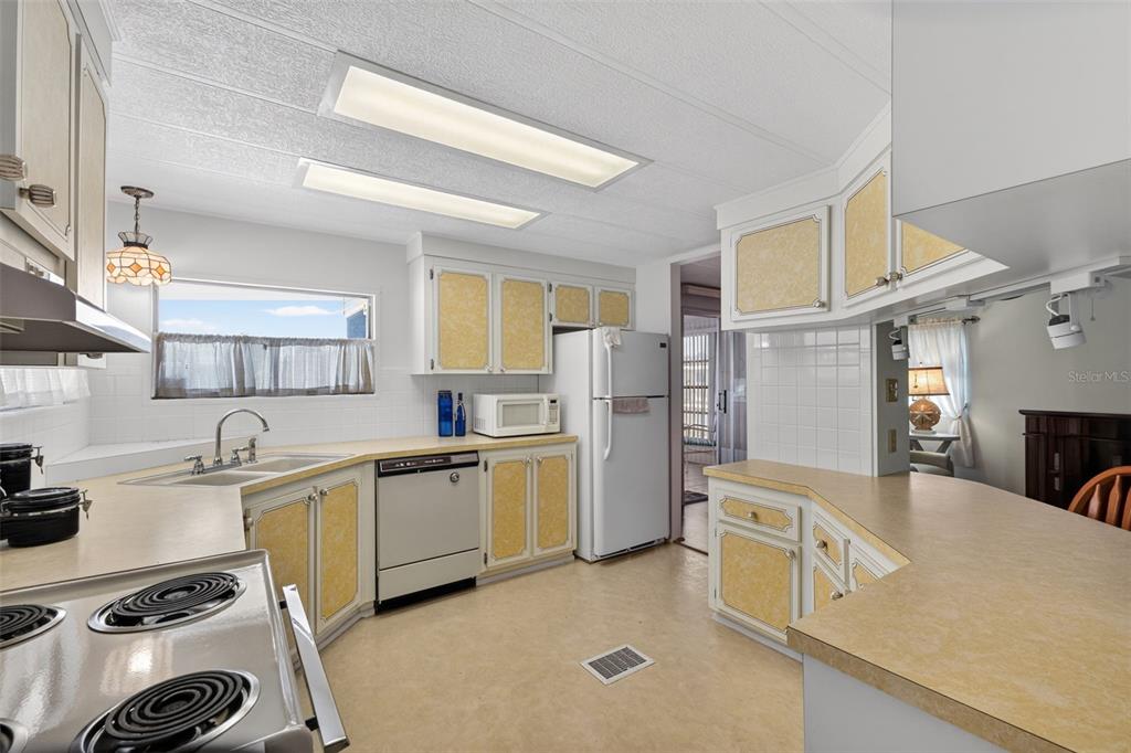 A kitchen features yellow-trimmed cabinets, laminate countertops, white appliances, and two rectangular ceiling lights — 322 ROBALO, NORTH PORT, FL