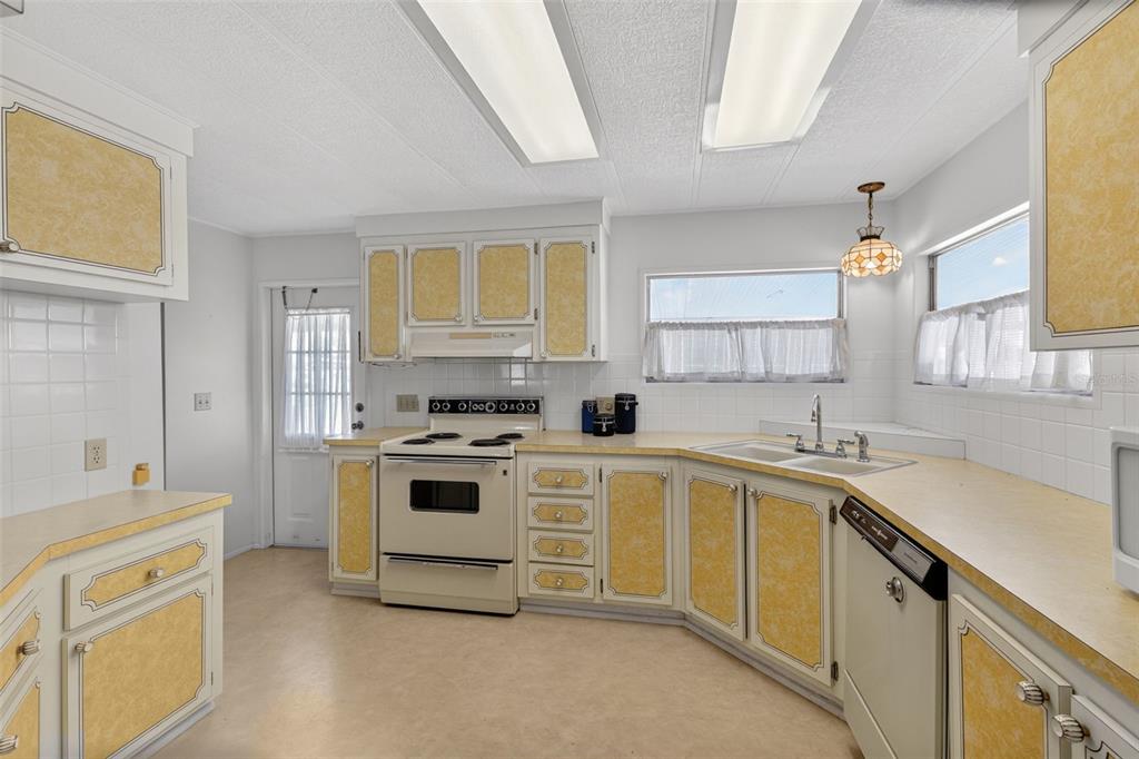A kitchen features yellow-paneled cabinets, white appliances, laminate countertops, and two large ceiling light fixtures — 322 ROBALO, NORTH PORT, FL