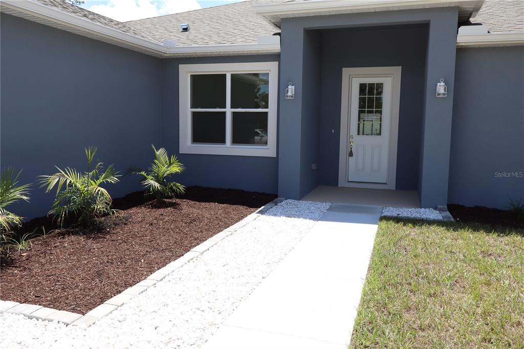 A gray house exterior features a white front door, a paved walkway, and landscaped mulch beds — 324 CONDOR AVENUE, SEBRING, FL