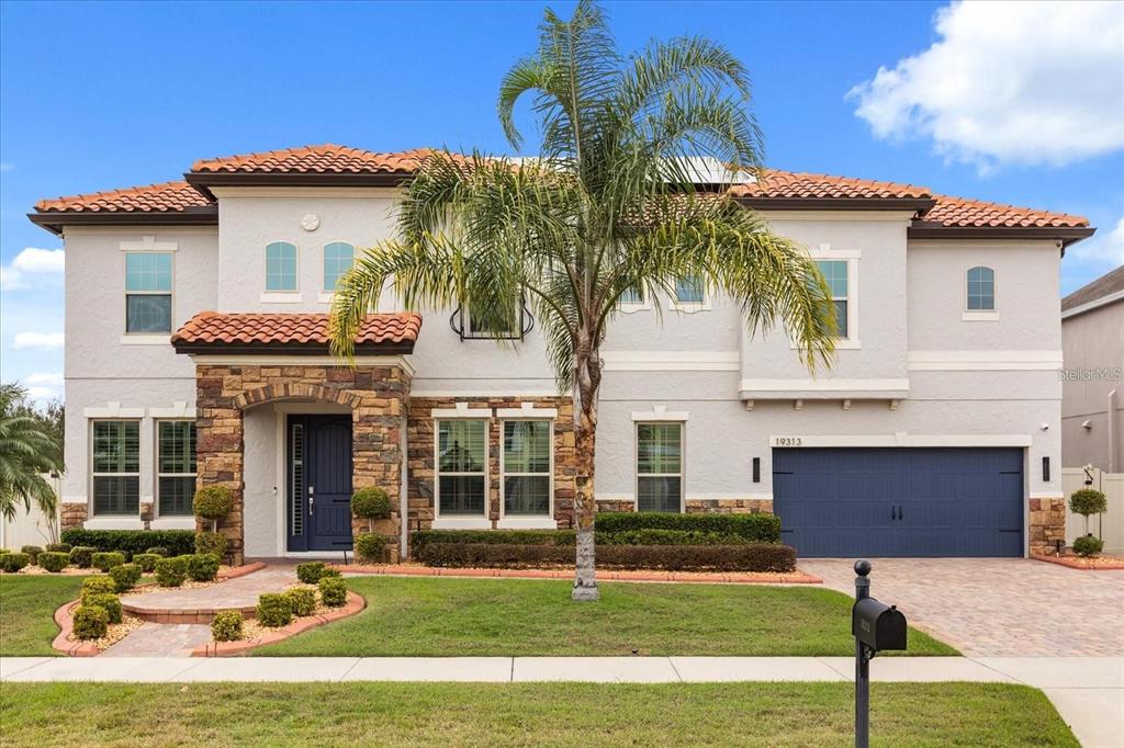 A two-story house with a stone-accented entryway, blue garage door, and a palm tree — 19313 PUMMELO DRIVE, ORLANDO, FL