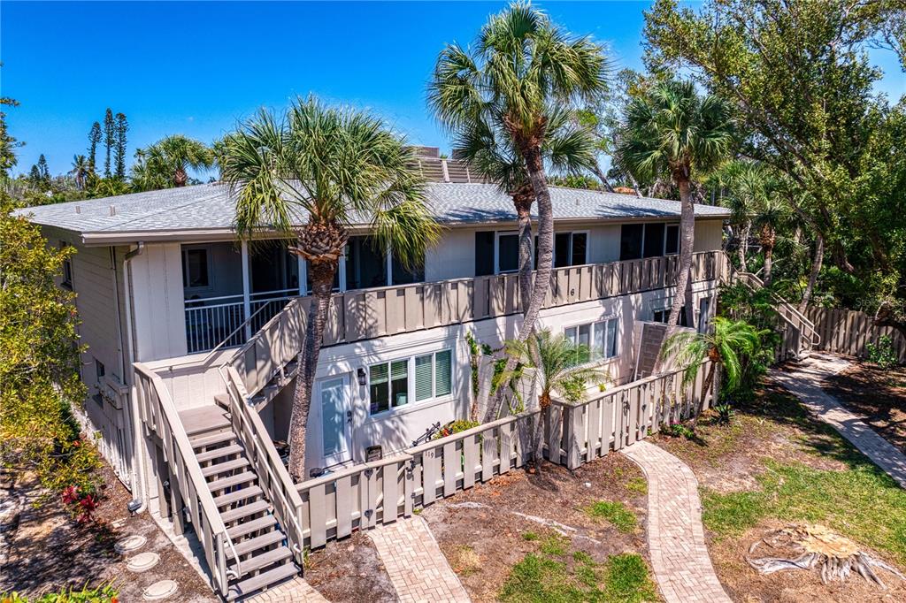 An exterior view of a two-story apartment building with wooden stairs, balconies, and palm trees — 6700 GULF OF MEXICO DRIVE UNIT 117, LONGBOAT KEY, FL